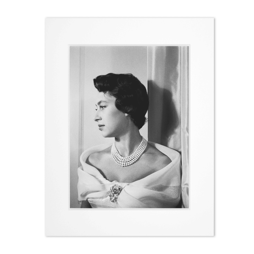 A black and white portrait photograph of a young Princess Margaret in profile wearing Cartier jewellery on a white scoop-neck dress